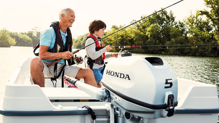 Un abuelo de pesca con su nieto en una embarcación con motor fueraborda Honda